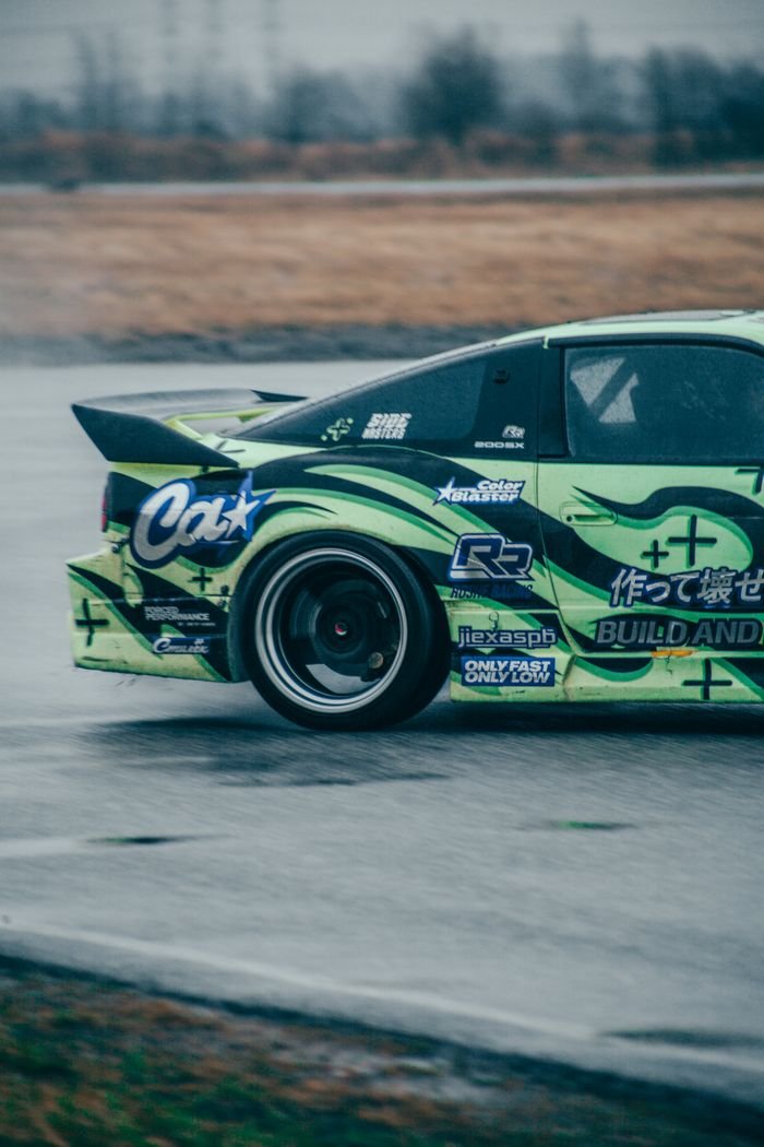 Close-up of a sports car drifting on a wet racing track, showcasing motion and speed.