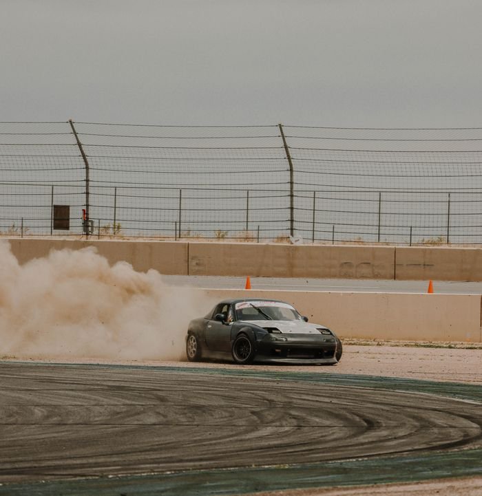 A sports car drifting smoothly on a race track, kicking up dust during a motorsport event.