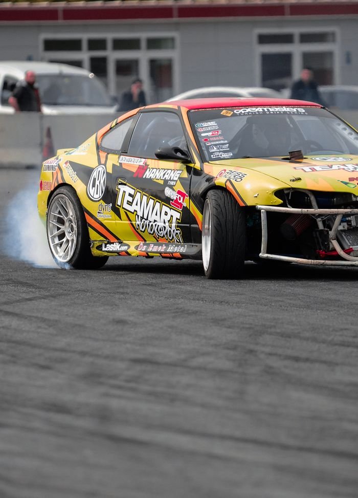 A vibrant drift racing car skids on asphalt, creating smoke.