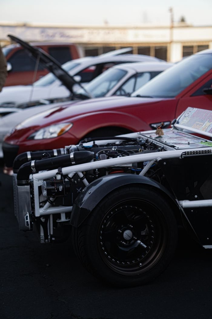 Close-up of sports cars with open hoods at a car show, highlighting vehicle design.
