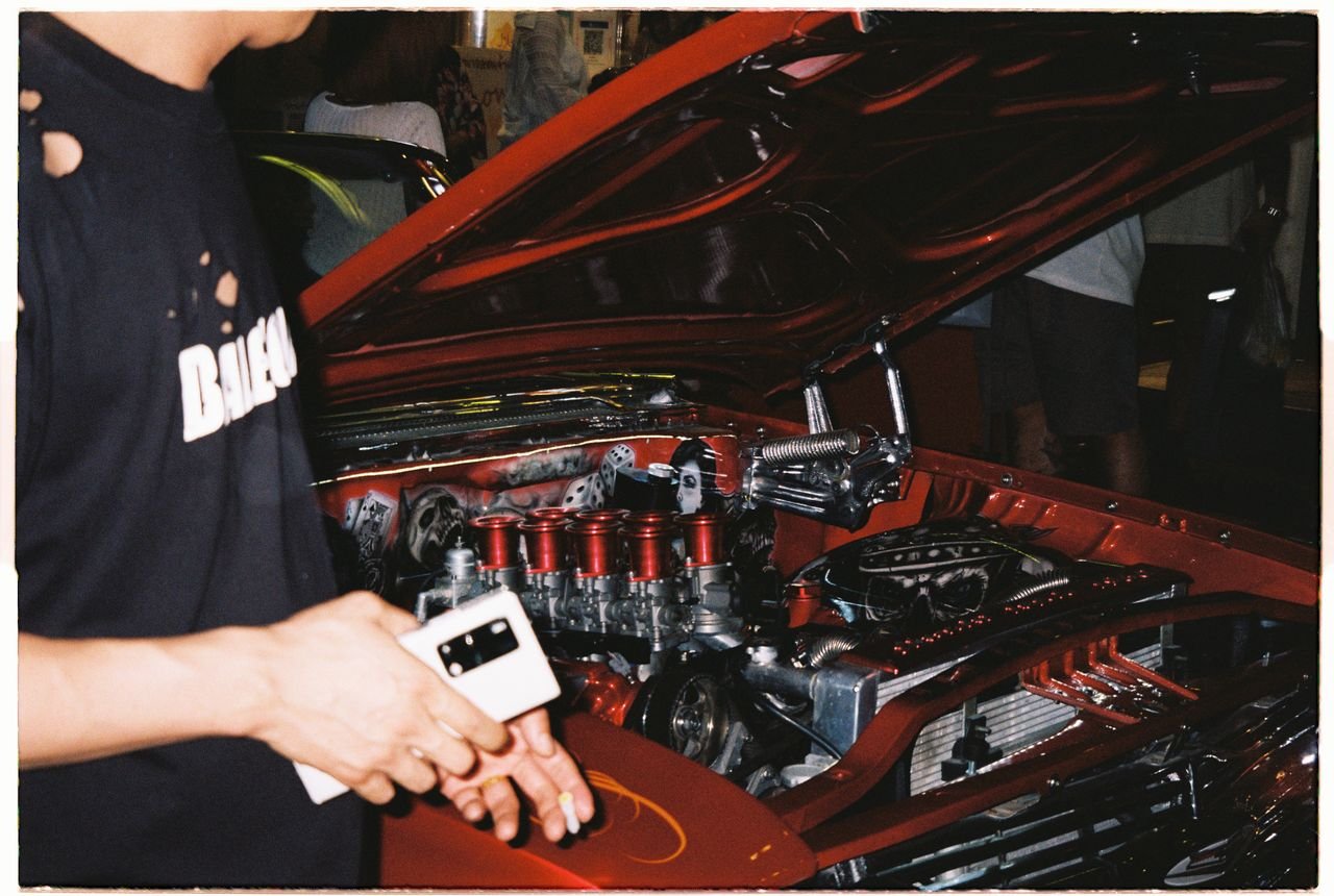 social-feed-img-03 A vibrant shot of a customized car engine with enthusiast holding phone, showcasing intricate details.