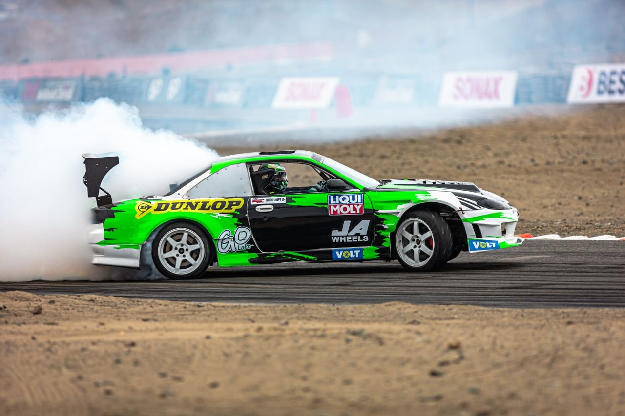 social-feed-img-02 High-adrenaline shot of a green drift car speeding on a track, producing thick smoke.